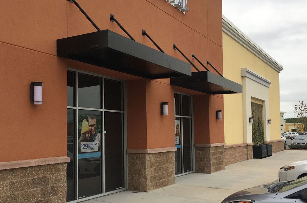 Black metal canopies on brackets over storefront entrances on an orange building