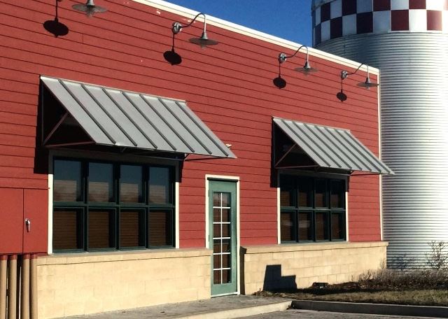 Gray standing-seam metal awnings over windows on a red building